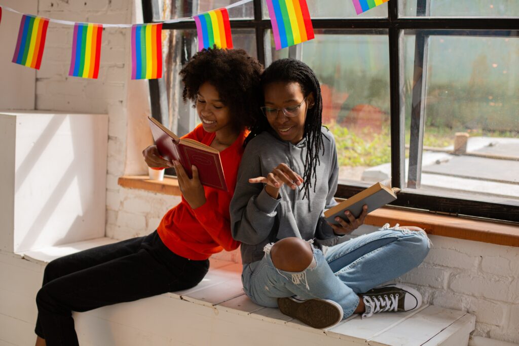 two people sitting on the floor, with rainbow flag decoration around them in a room